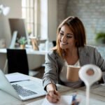 Happy businesswoman writing notes while working on laptop in the