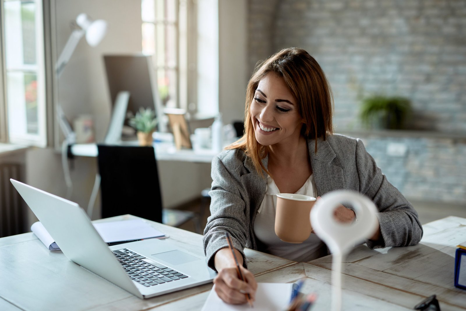 Happy businesswoman writing notes while working on laptop in the