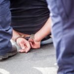 Midsection Of Prisoner Sitting On Street Surrounded With Police Force