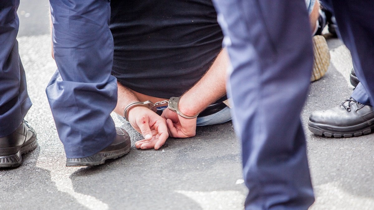 Midsection Of Prisoner Sitting On Street Surrounded With Police Force